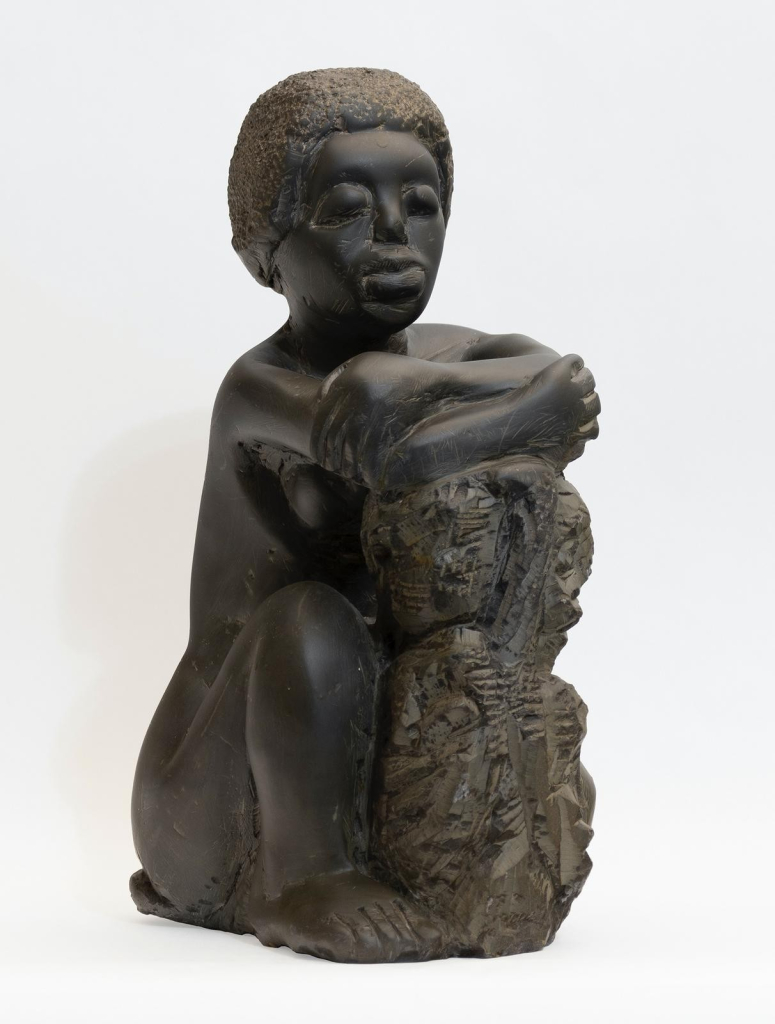 Black stone sculpture of a Black woman sitting with her knees up, arms resting against an abstract structure