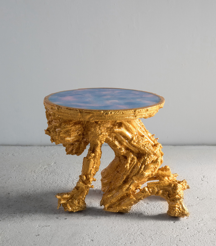 Small gold table with a top resembling a cloudy sky and a gold base in the form of a textured, crouching figure