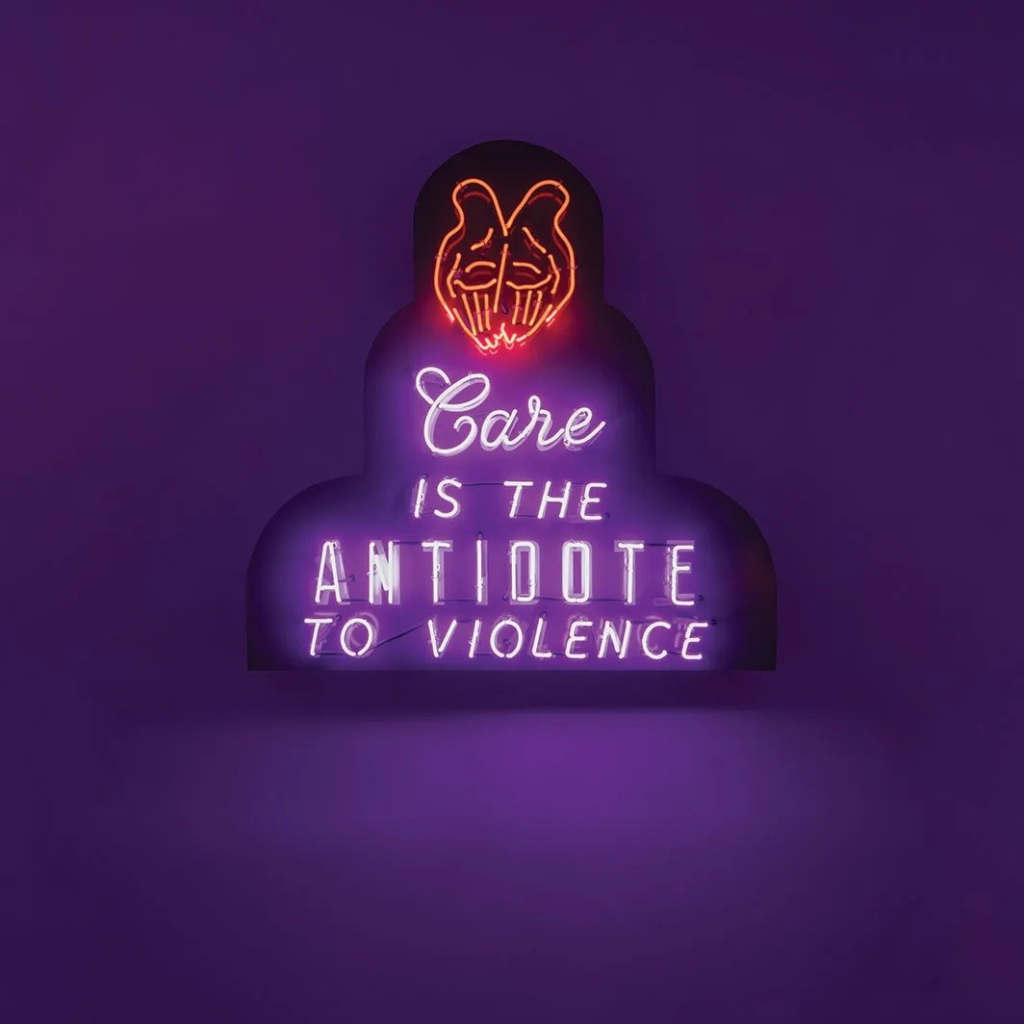 Neon sculpture with the text "Care is the antidote to violence" against a purple wall