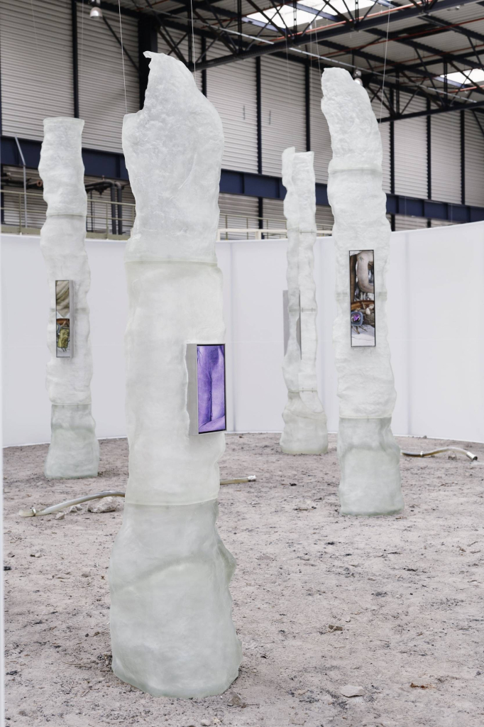 Several tall standing sculptures in opaque white with textured tops and various photos attached to the their centers