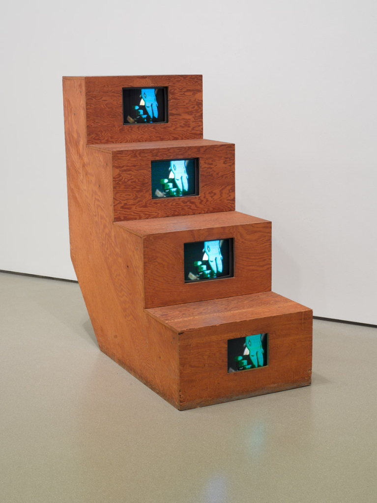 Wooden sculpture of a set of 4 steps, with a video screen inlaid in each step showing a nude, a riff on Duchamp's "Nude Descending a Staircase"