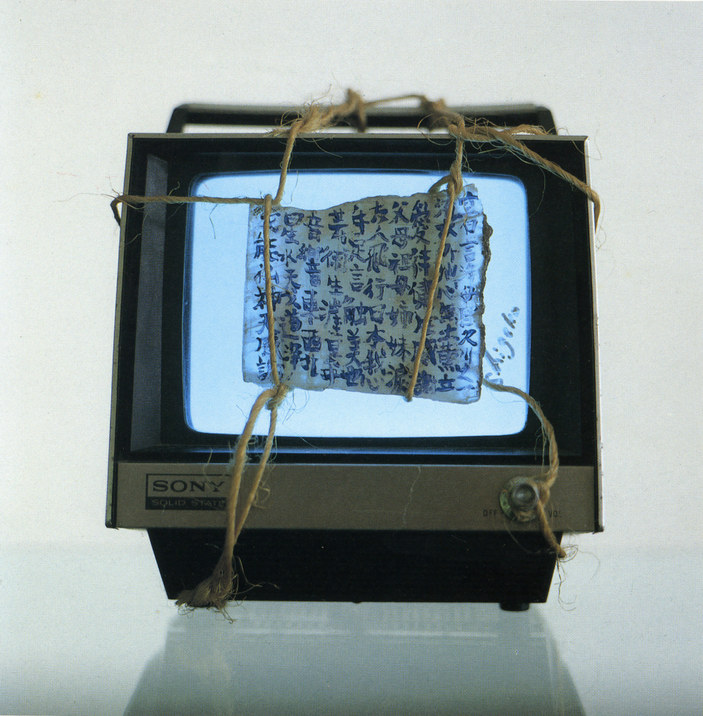 A small square sony tv, with a sheet of parchment with kanji calligraphy written in ink and held over the white screen by twine