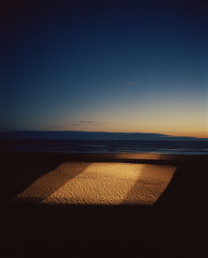 Vertical photo of a beach at twilight, with a large square patch of sunlight on the sand