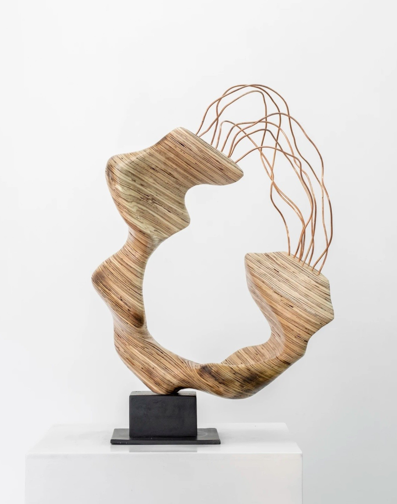 Wooden sculpture of a curving C-like shape with copper wires spread between the two ends