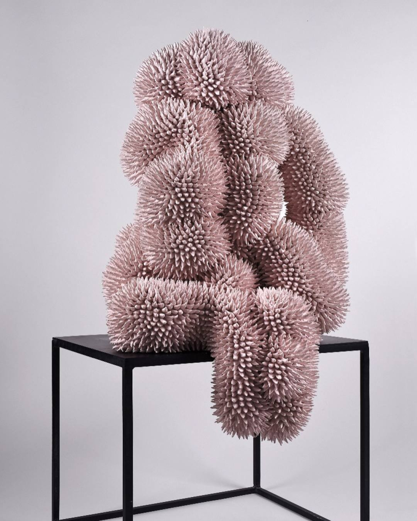 Abstract sculpture of a dusty rose-colored biomorphic shape covered in prickly points, sitting atop a table