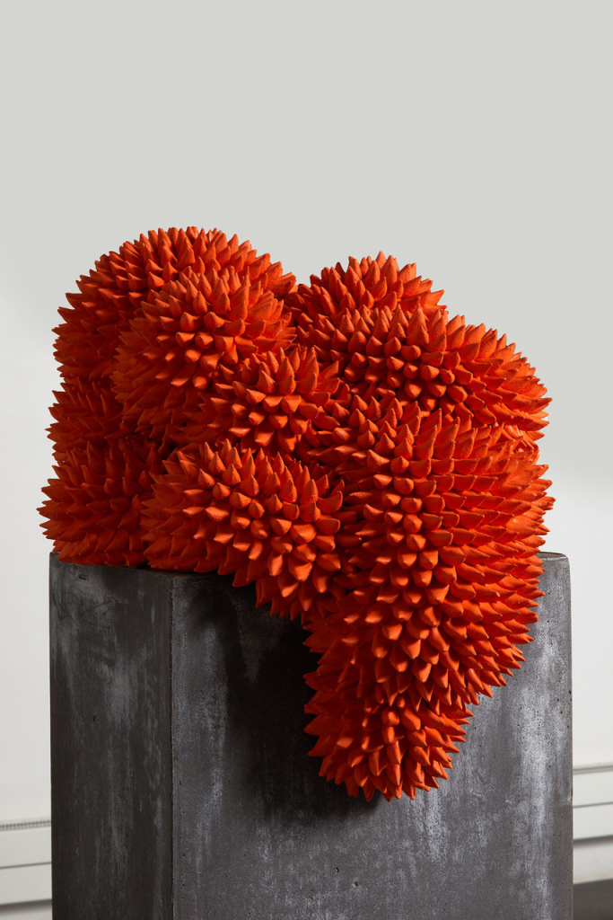 Abstract sculpture of a bright red biomorphic shape covered in prickly points, sitting atop a concrete block