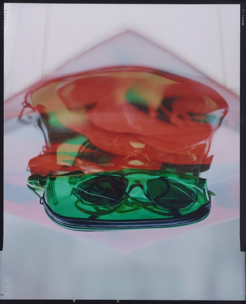 Semi-abstract photo of a clear green glasses case holding sunglasses and a blurry red shape behind it