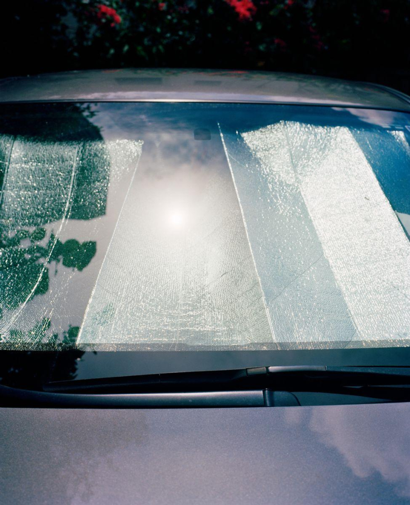 Photo of a car windshield with a metallic screen in the window reflecting bright sunlight