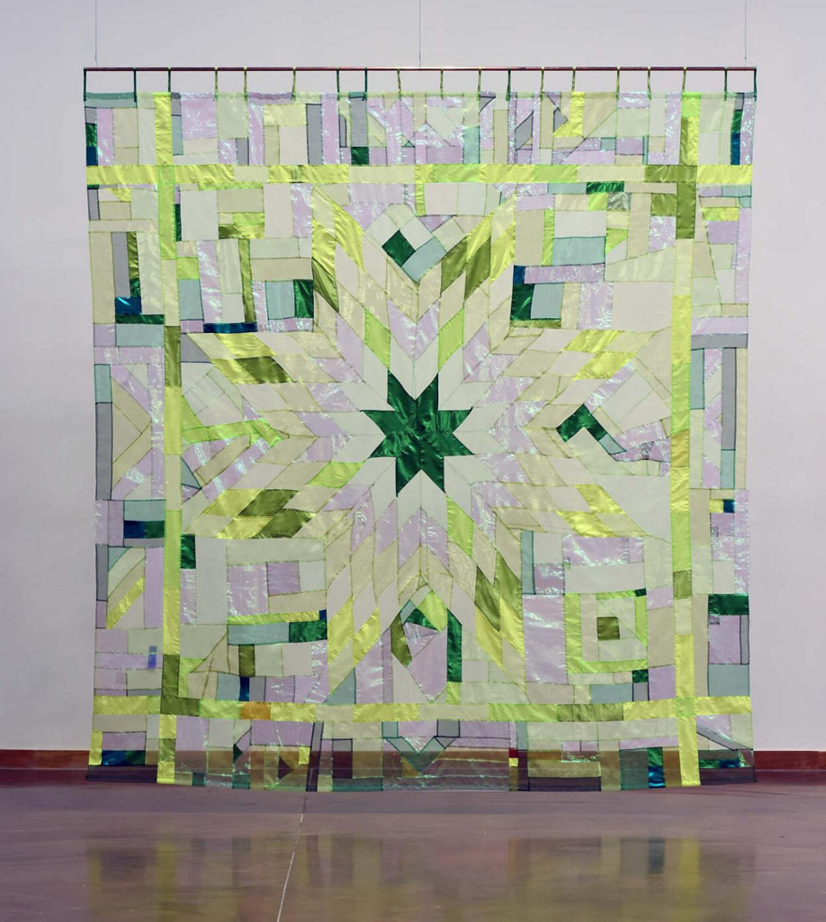 Hanging quilt with a star pattern in a green palette, using shiny and transparent fabrics