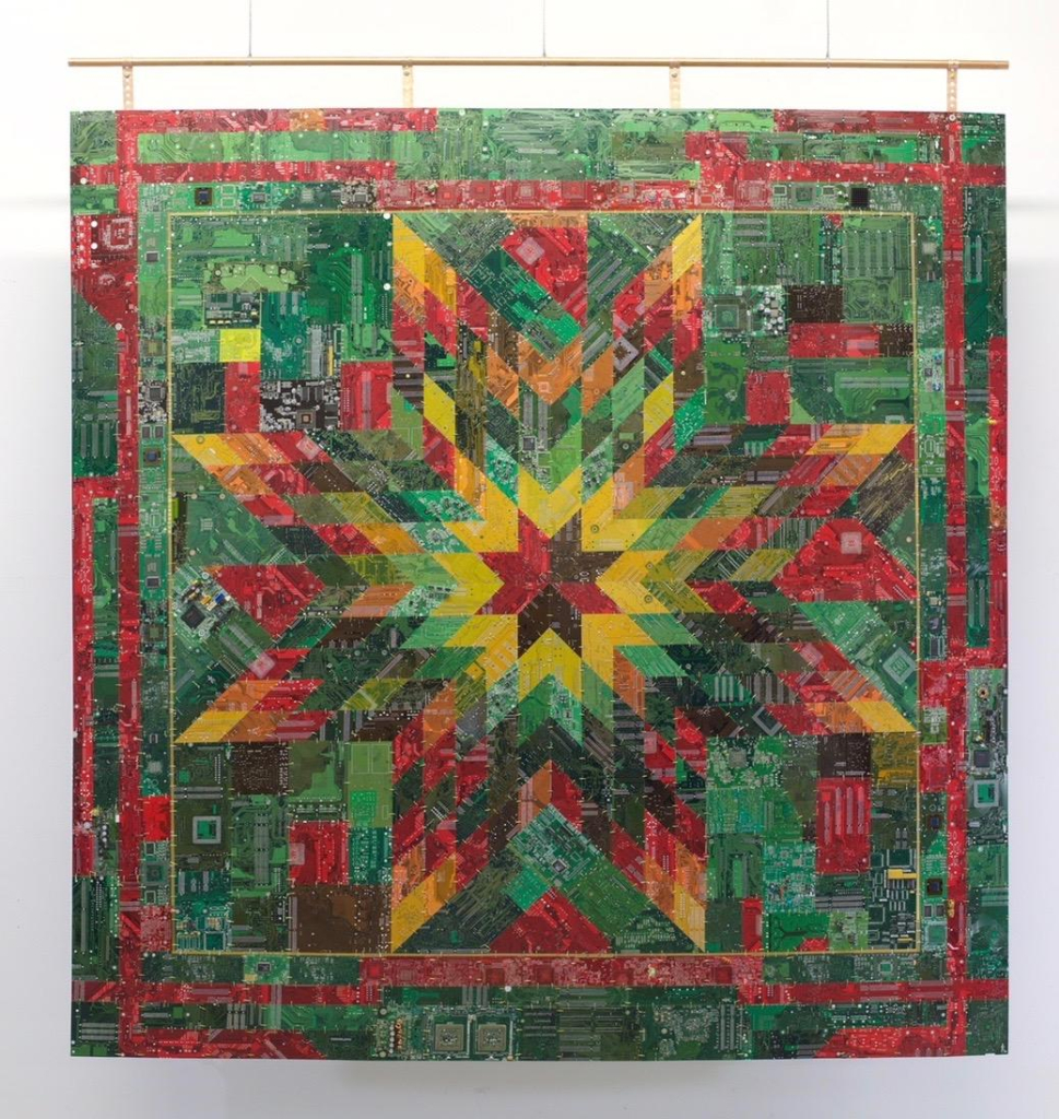 Hanging quilt with a star pattern in a green, red, and yellow palette, made with circuit boards