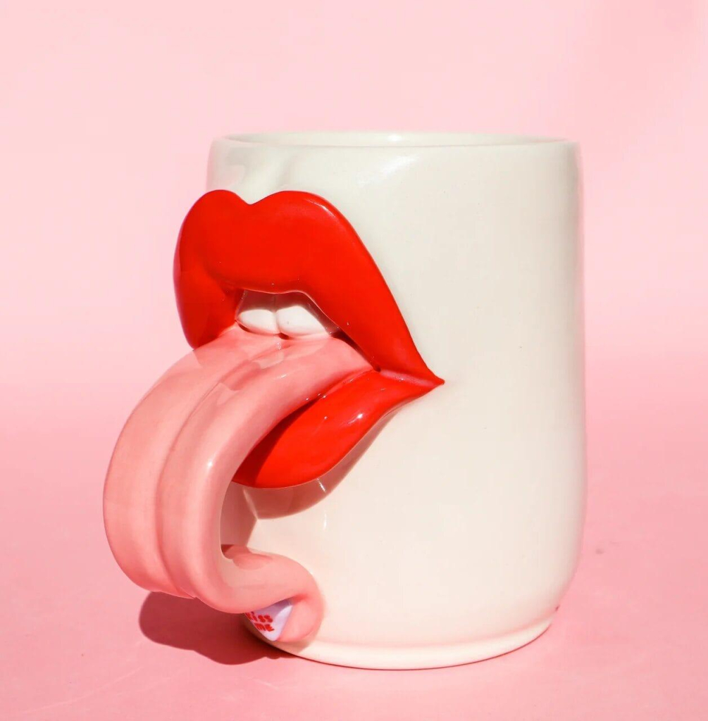 Ceramic vessel with large sculpted red lips sticking out a long pink tongue that curves like a handle