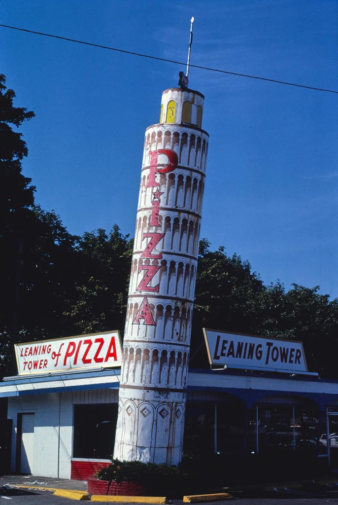 Photo of "Leaning Tower of Pizza" restaurant with a slender leaning tower sculpture decorated with narrow archways and vertical text reading "PIZZA"