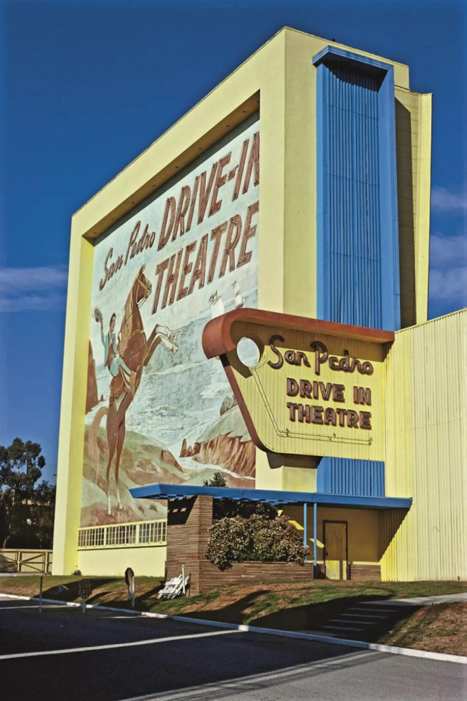 Photo of San Pedro Drive-in Theatre building, painted bright yellow and blue with a mural of a man riding a horse and waving