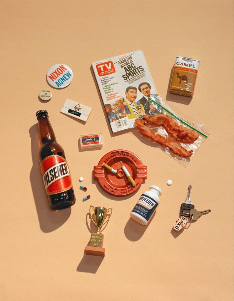 Still life photo of a collection of items arranged on an orange cream background, including a TV Guide, Nixon button, bacon, pills, and car keys