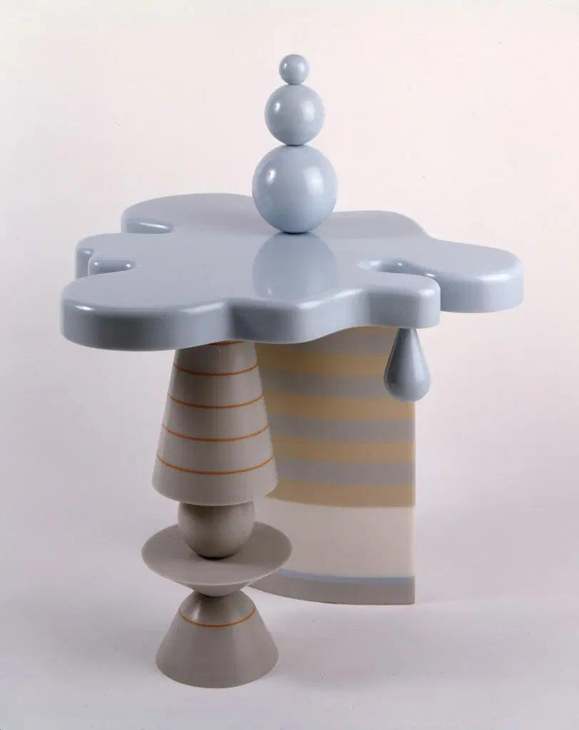 Table with abstract striped legs and light grey-blue top with curving edges resembling a cloud or puddle of water