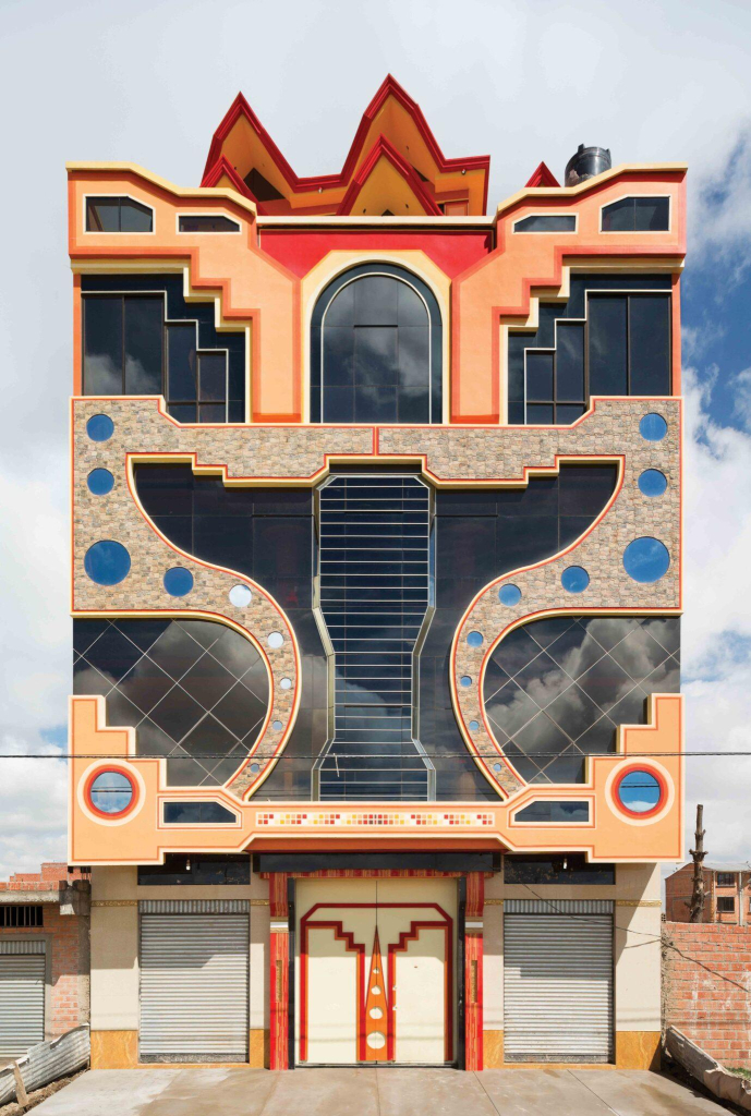 A vertical building with bold geometric facade in peach, red, grey, and blue colors and symmetrical design. The central motif resembles an abstract bird with wings spread wide on either side.