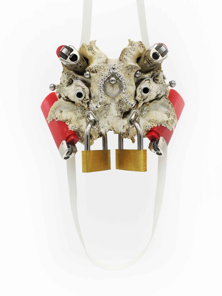 A symmetrical pendant featuring lighters, padlocks, and metal balls set within a white piece of coral and strung on a white ribbon