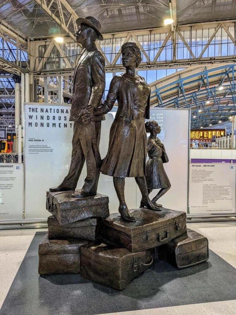 Bronze monument to the Windrush Generation, depicting a Black man, woman, and child standing together in confident poses on top of piles of suitcases