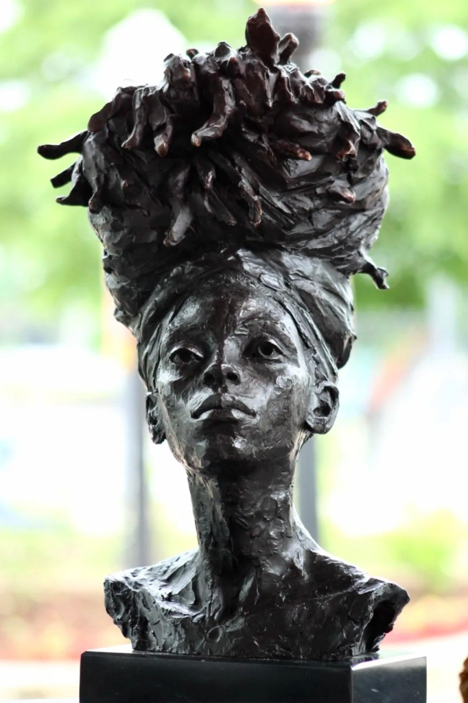 Bronze sculpture bust of a young Black woman wearing a headwrap with her hair piled high resembling organic tubers or stems