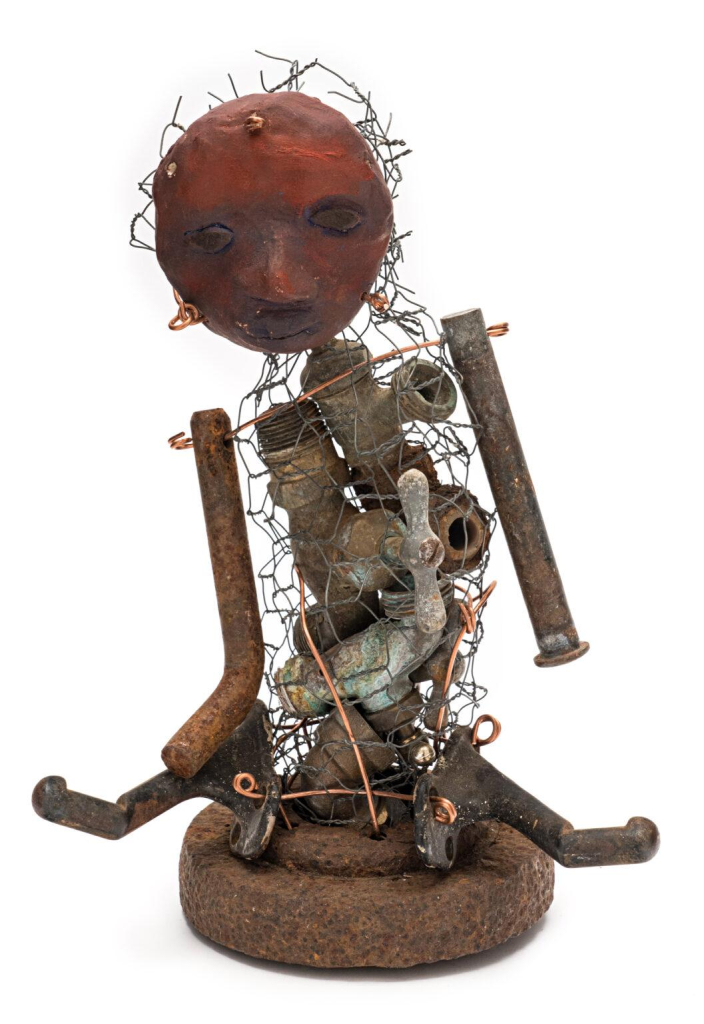 Sculptural figure made up of rusty metal parts and barbed wire, with a red clay face