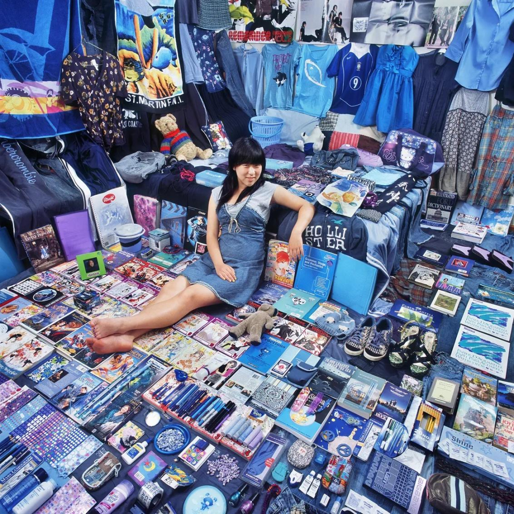 Photo of a teen girl sitting on the floor of her room with all of her blue and purple possessions laid out around the floor, walls, and bed