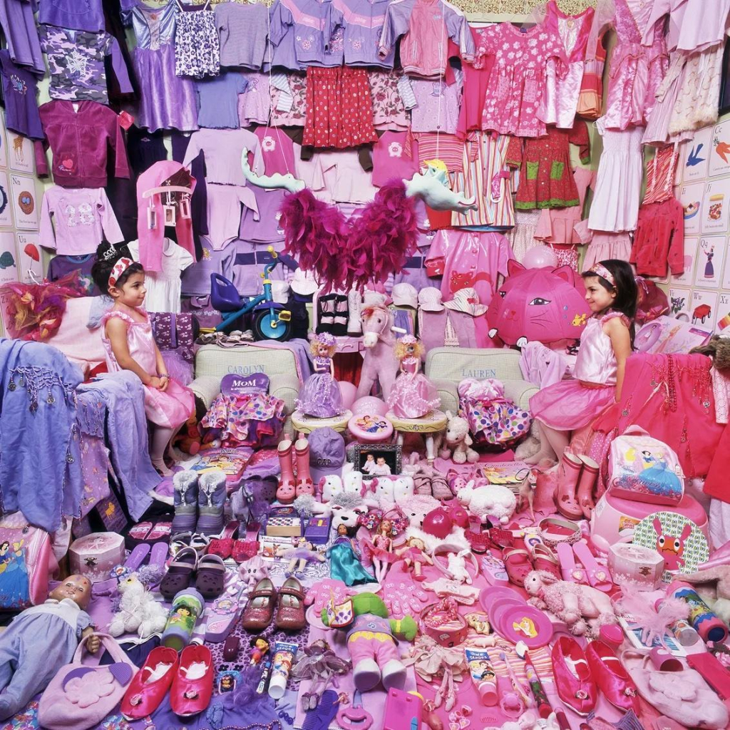 Photo of two little girls sitting on their beds facing each other, with one half of the room covered in pink items and one covered in purple.