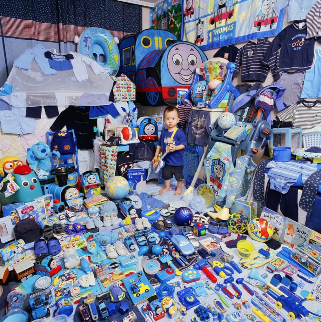 Photo of a little boy standing in a corner of his room, surrounded by all of his blue possessions spread out along the floor and walls