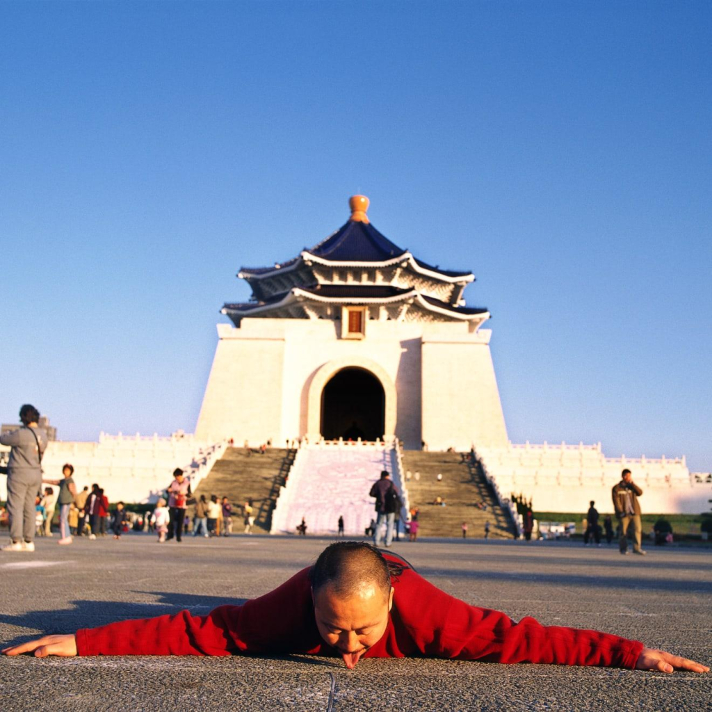 Photo of the artist in Taipei lying prostrate on the ground with his tongue licking the pavement, in front of a white temple