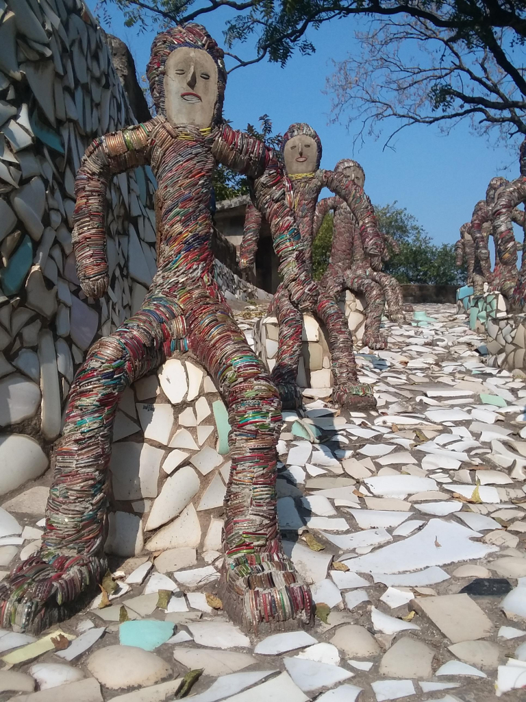 Figures made of small, colorful fragments, all seated on bumps erupting from a ground decorated with green- and sand-colored stone stiles