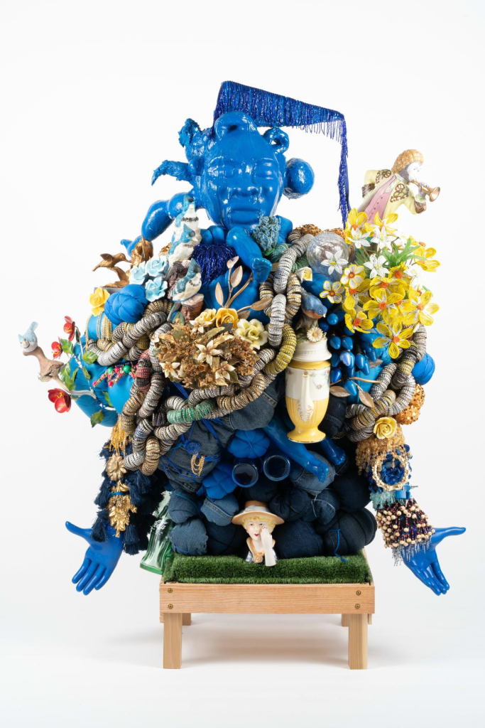 Sculpture of a blue female figure whose body is covered in flowers and textiles