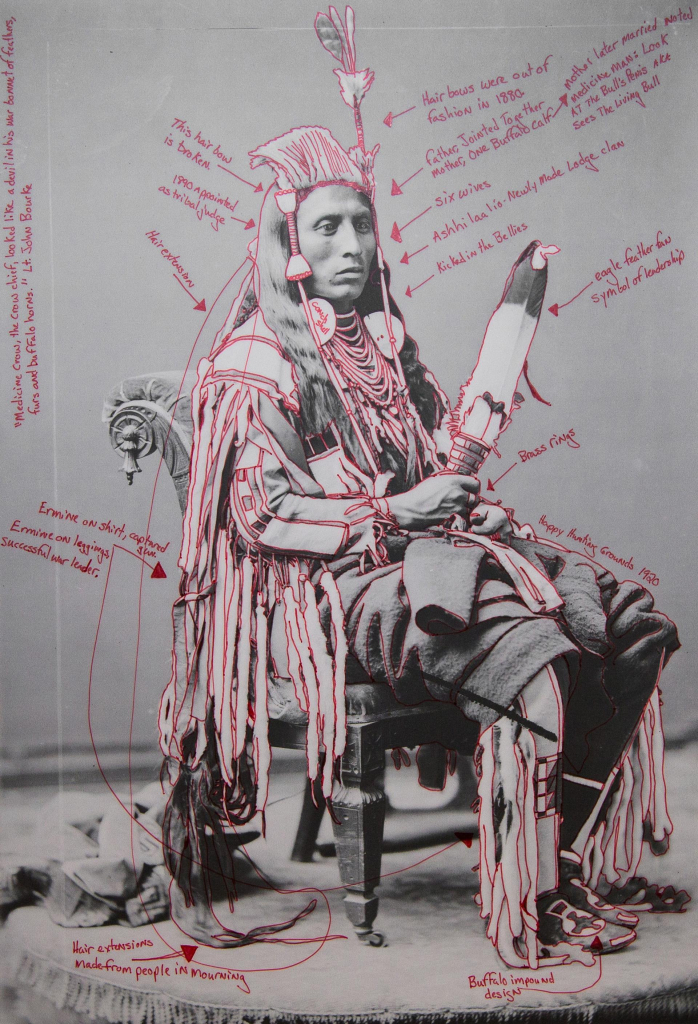 Black and white photo portrait of a Crow chief, with notes in red pen added identifying different aspects of his clothing and additional symbols, along with some hypothetical observations