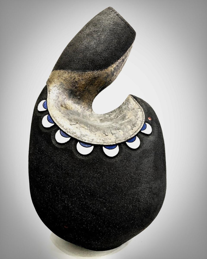 Ceramic form with a rounded base and curving hook-shape top, decorated with crescent-moons and a dark textured overlay