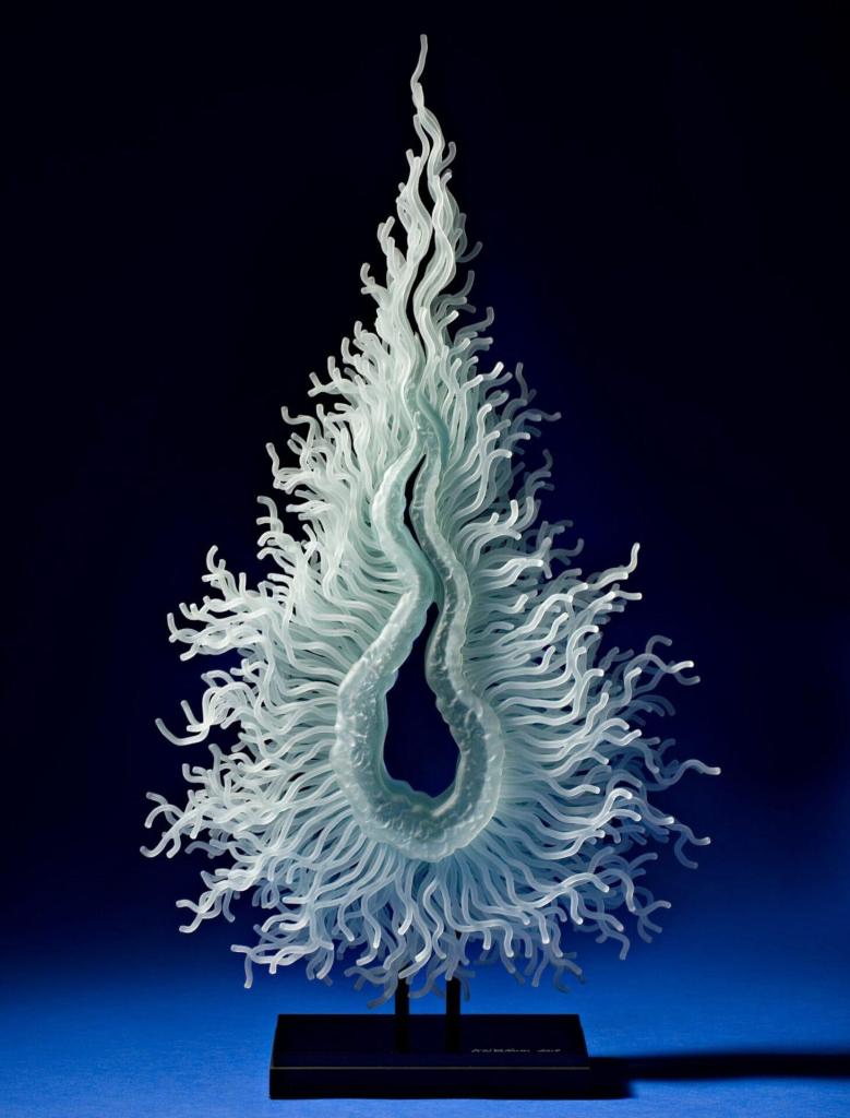 Glass sculpture made up of thin, wavy glass tendrils radiating outward from a droplet-shaped center, resembling a small fire