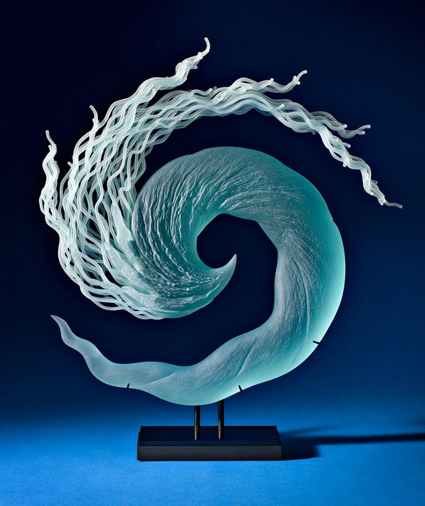 Glass sculpture of a curving spiral shape resembling a wave, with wavy tendrils coming off the top like surf