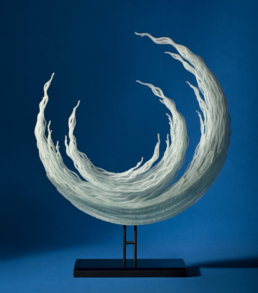 Glass sculpture of two crescent moon shapes with wavy tendrils, one smaller held within the other. 