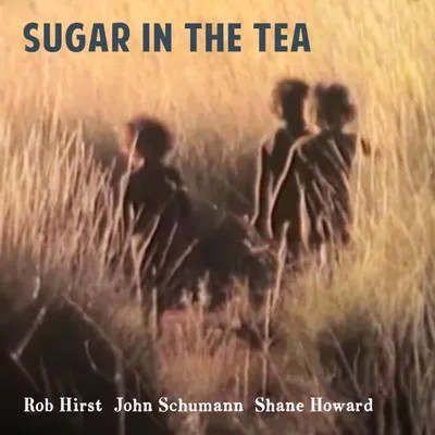 Image shows three little Australian Pintupi children moving through the tall pale golden-brown spinifex of the dry country. The title ‘Sugar in the Tea’ appears in text across the top. The musicians’ names are printed below: Rob Hirst, John Schumann, Shane Howard.