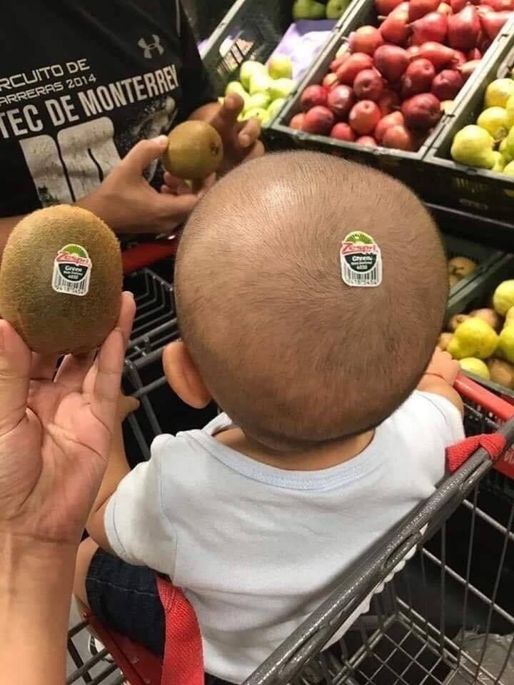 a man holding a kiwi with a fruit sticker next to a baby's head with a fruit sticker on it