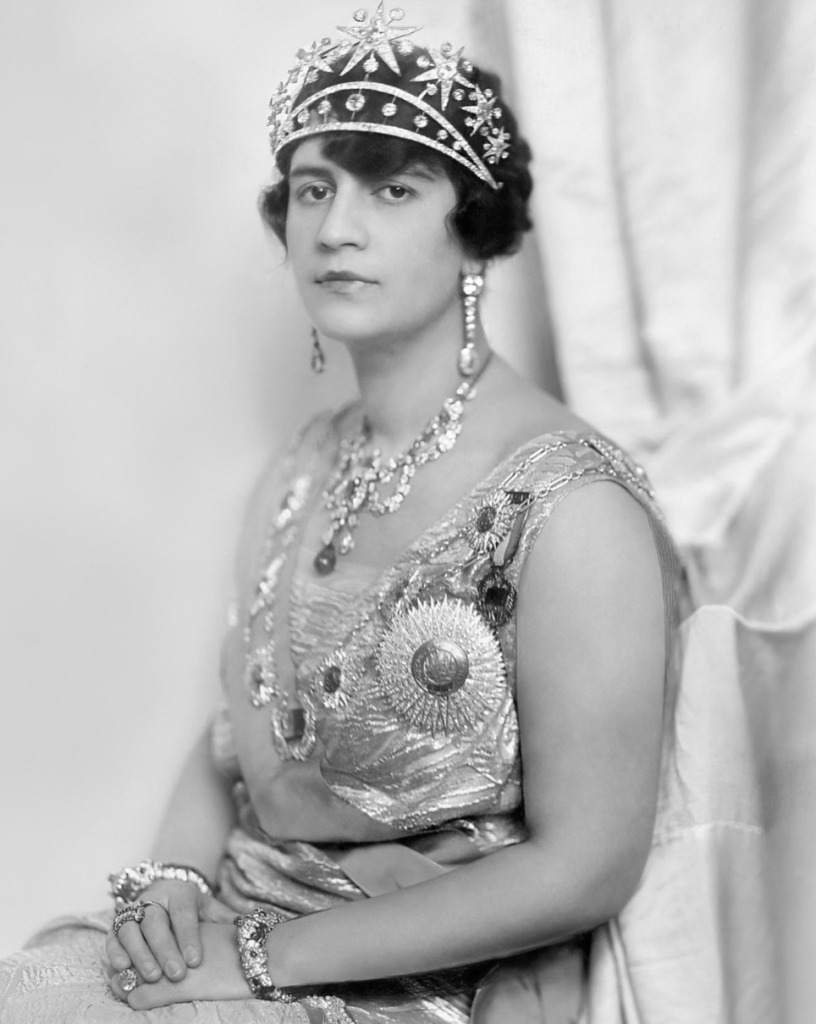 Portrait photo of queen Soraya of Afghanistan in 1919. She has a modern 'bob' haircut, is wearing a tiara and necklace, and an embroidered off the shoulder silk dress