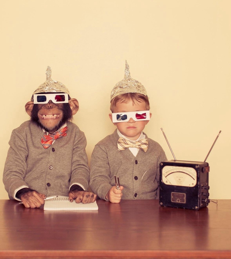 chimp and a boy wearing grey suits, 3-D glasses and tinfoil hats with a Geiger counter and notepad