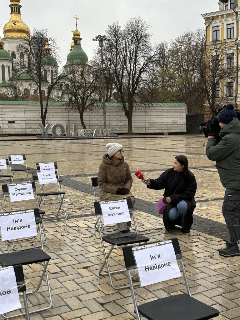 A formerly imprisoned artist has taken her seat and is being interviewed by a journalist. 