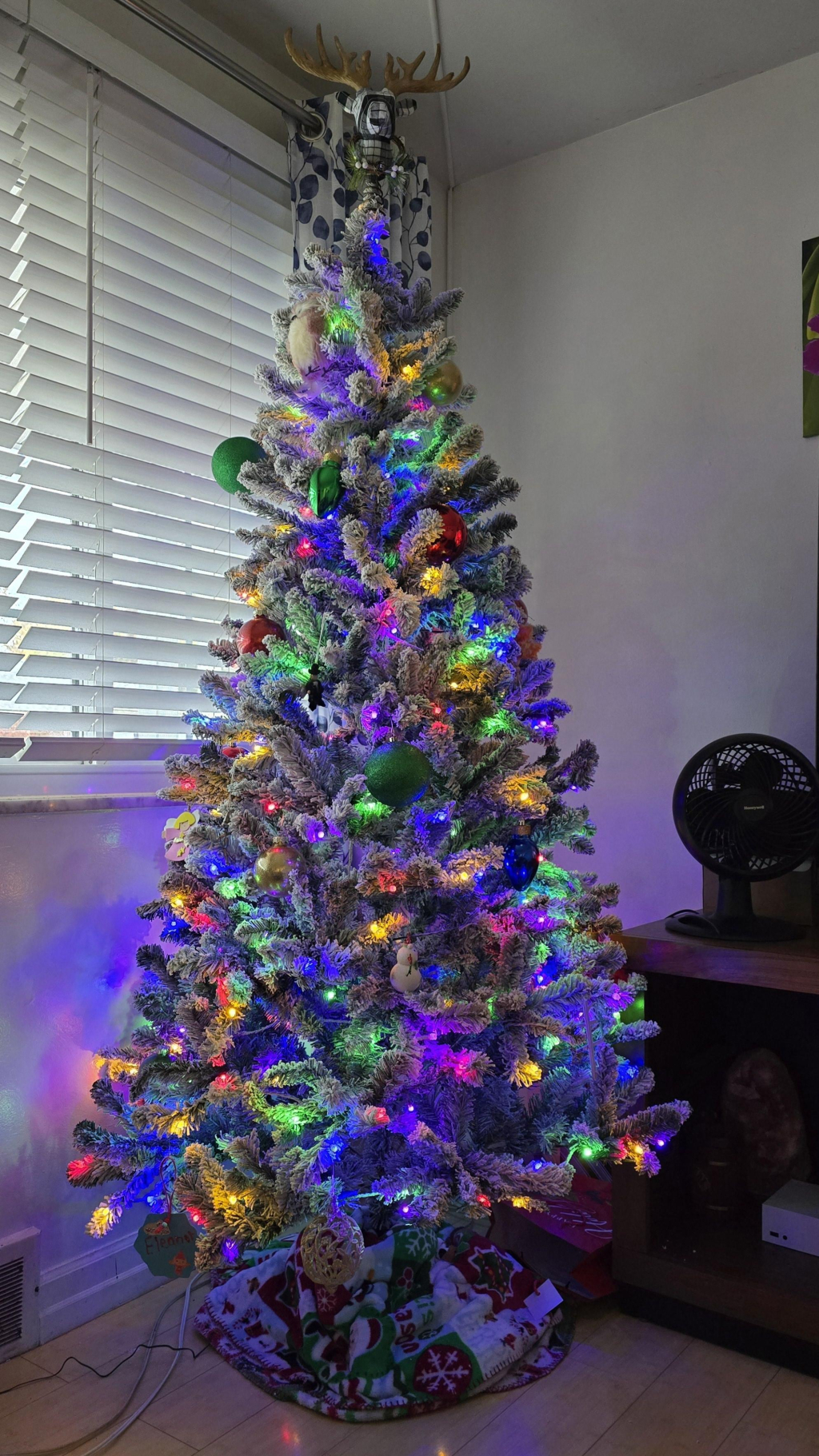 A flocked and multi-colored lit Christmas tree. The tree topper is a deer.