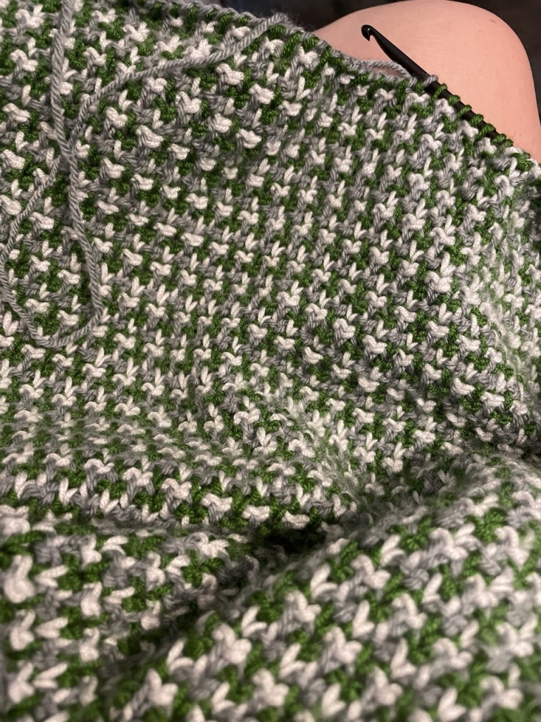 A Tunisian crochet baby blanket in the works in colors green, medium gray and light gray alternating in each row