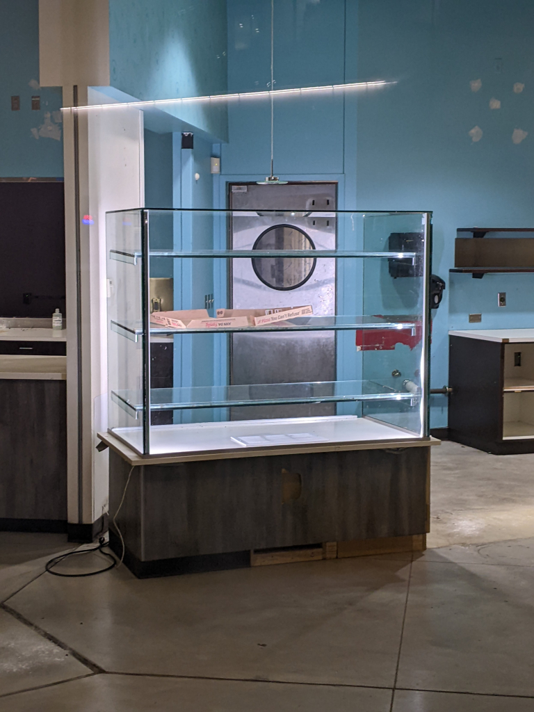 A lit display case in an empty storefront holds an empty pizza box.