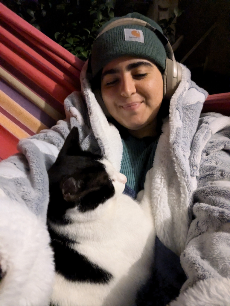 A selfie of me in the hammock in grey fluffy winter clothes and Oreo the cat on me I'm smiling