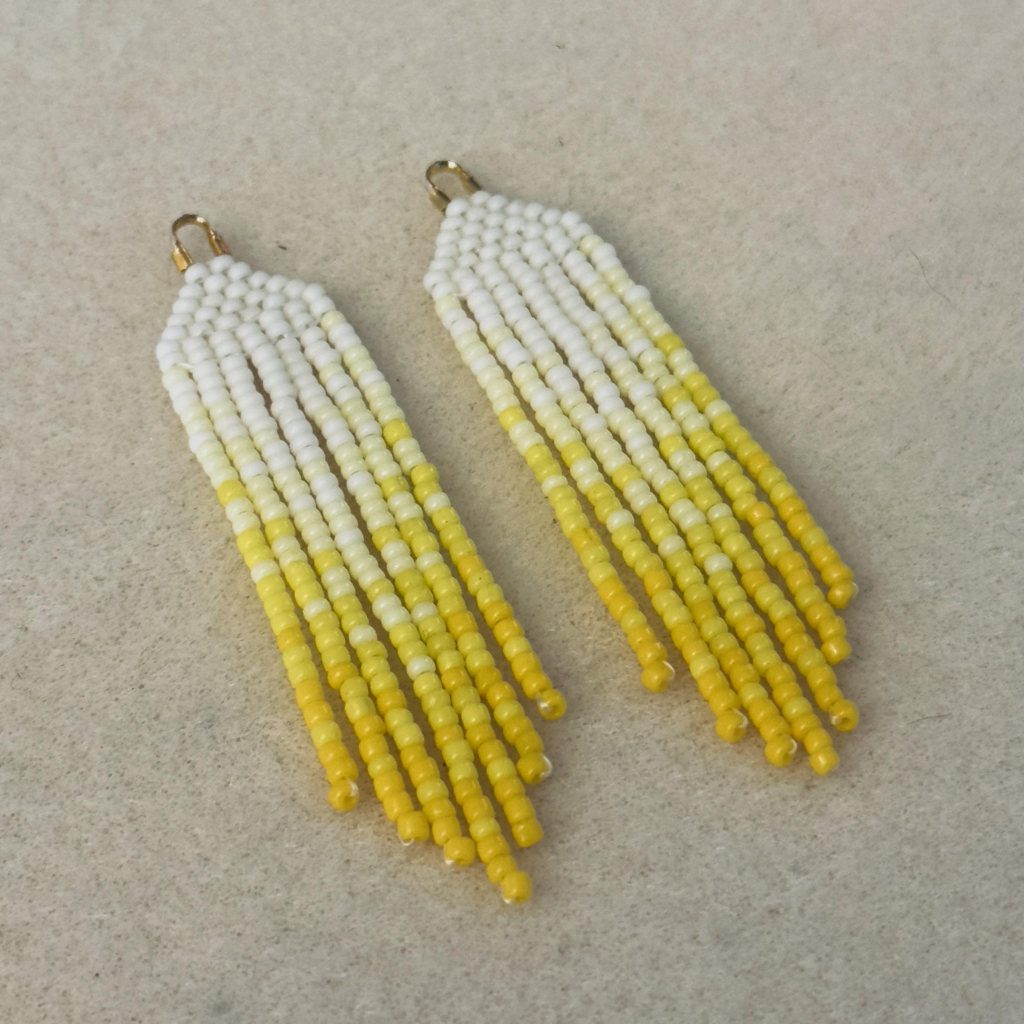 A pair of white to yellow ombre beaded fringe earrings on a bead mat