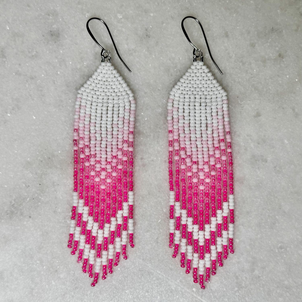 A pair of beaded fringe earrings on a marble background. They're ombre from white to hot pink, with white chevron stripes at the bottom.