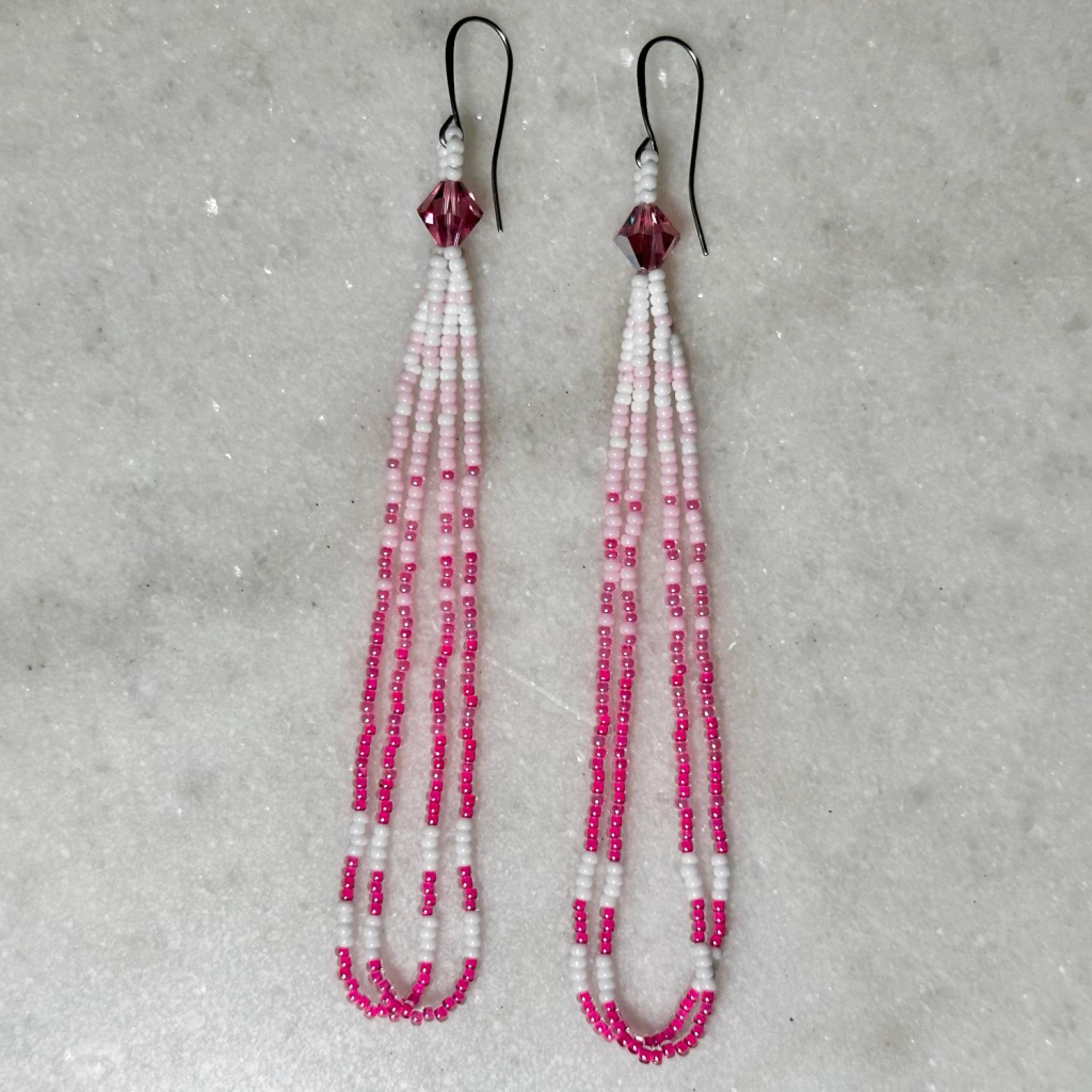 A pair of pink and white beaded loop earrings on a marble background