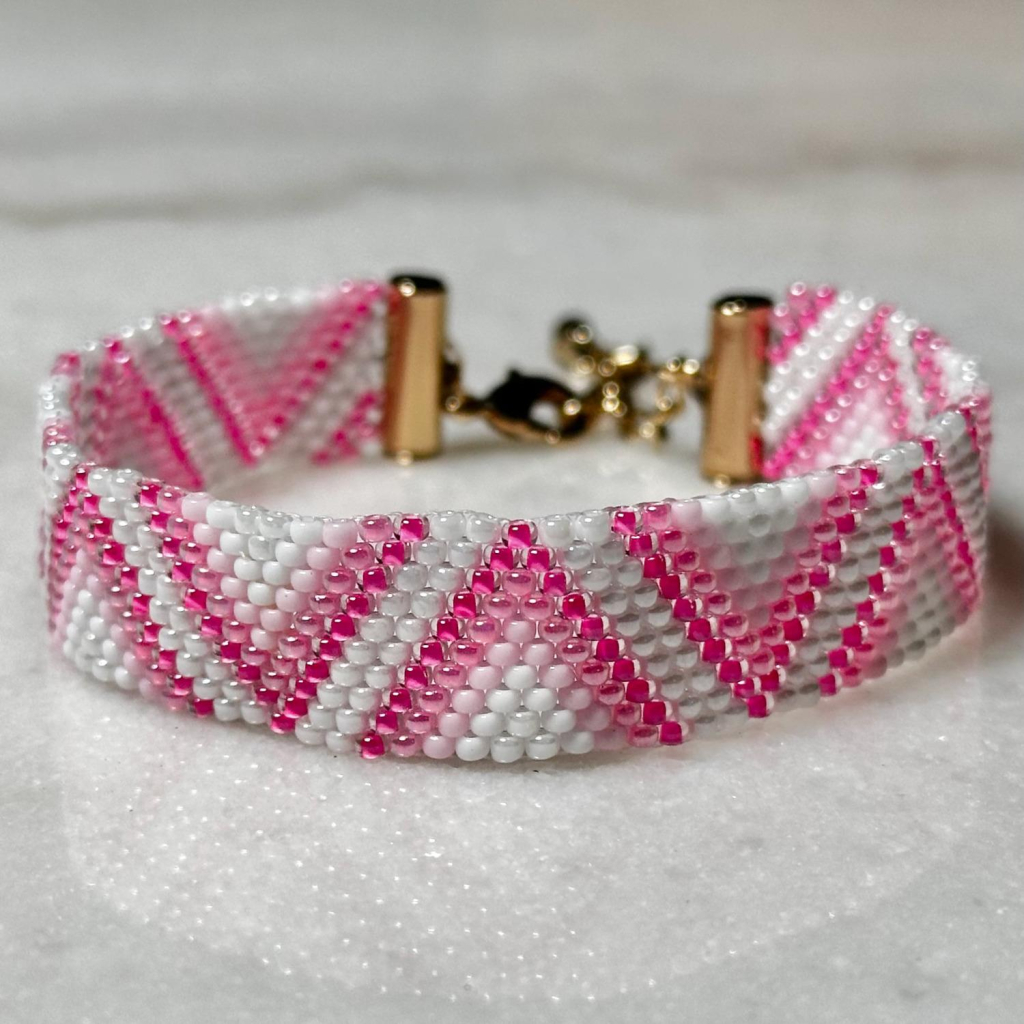 A triangle-patterned pink and white beaded bracelet with a gold clasp on a marble background