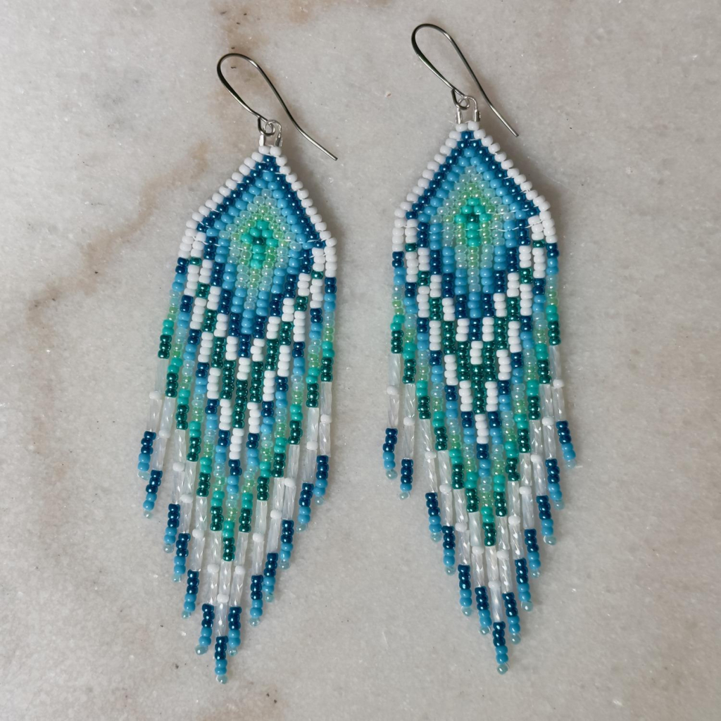 A pair of blue, turquoise, and white beaded fringe earrings on a marble background