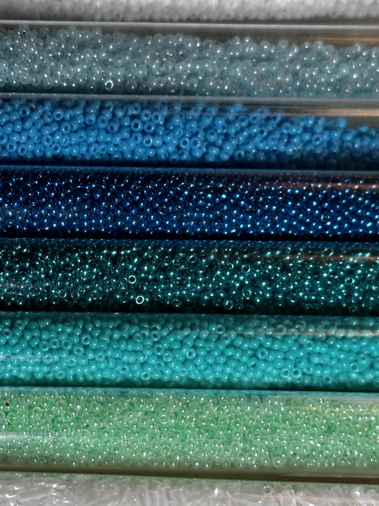 A lineup of tubes of blue and green seed beads